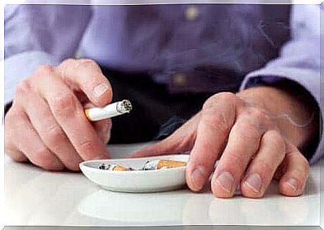 A man holds a cigarette over an ashtray