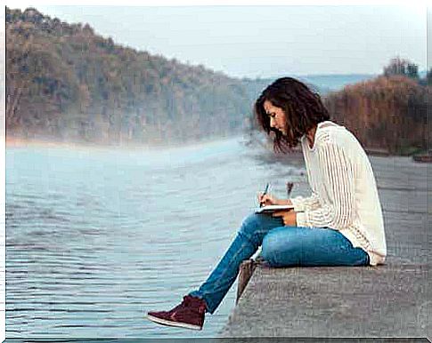 Woman sitting by the water writing